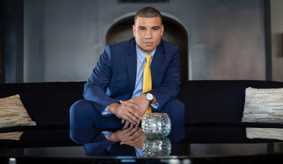 Man wearing blue suit and yellow tie sitting in a luxurious office.