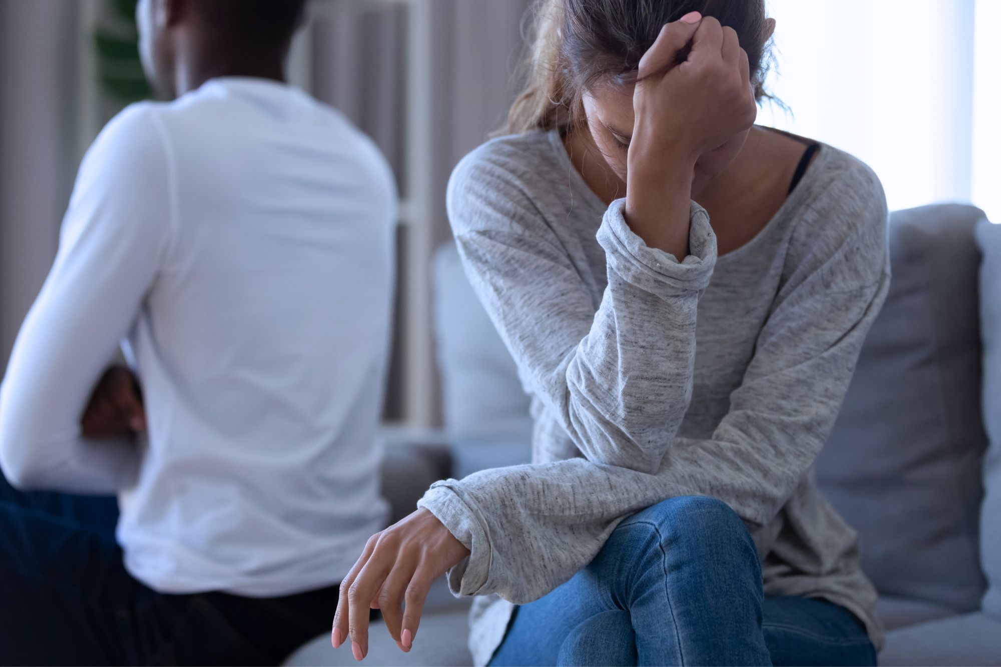 Husband and wife sit turned away from each other as the women cries, wondering why Infidelity Is So Painful To The Betrayed Spouse.