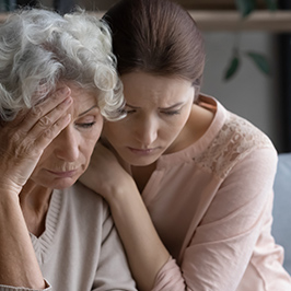 younger woman comforting older woman with hand on her forehead