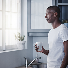 Man holding a cup looing out the window.
